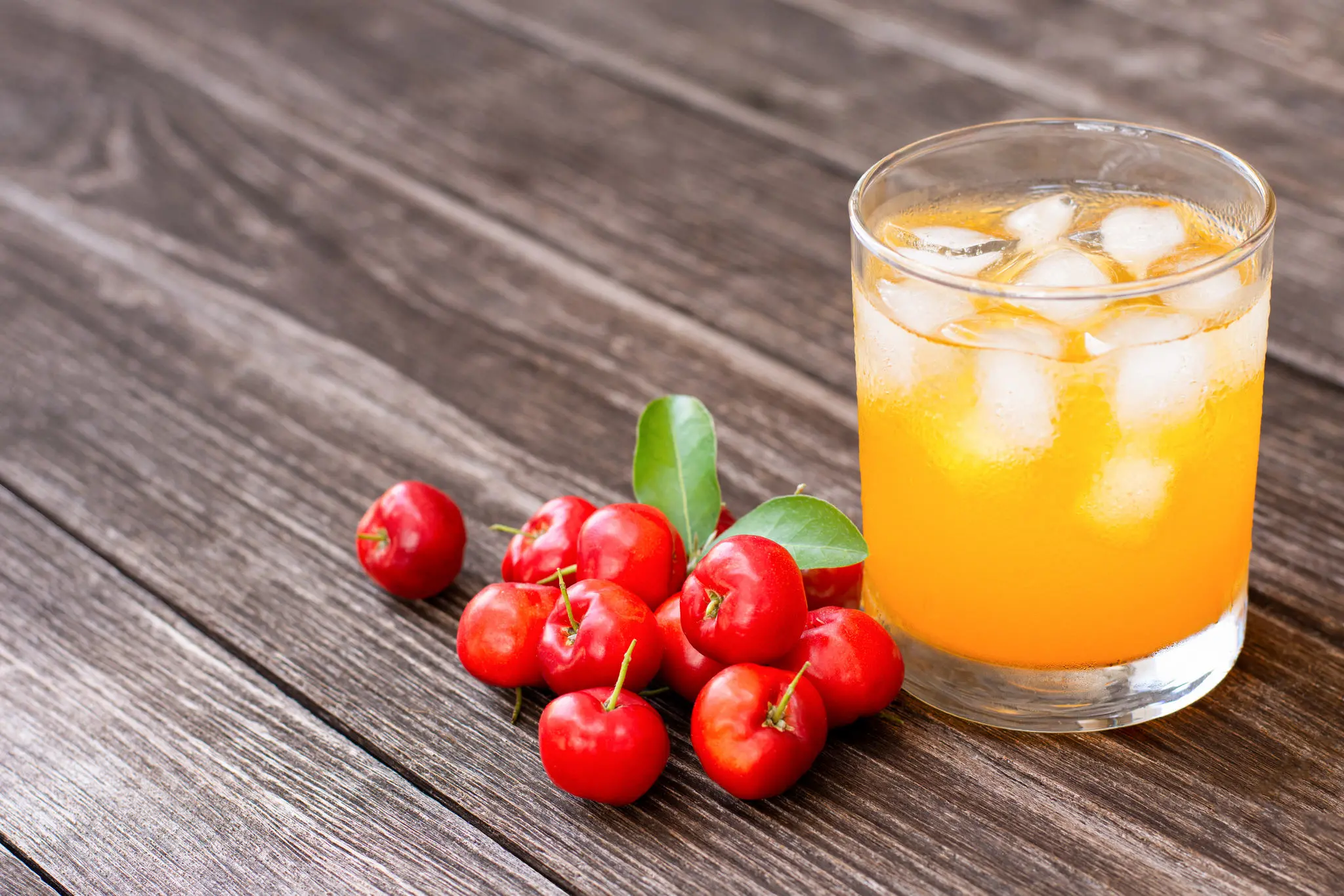 Copo com suco de acerola ao lado de alguns frutos sobre um fundo amadeirado