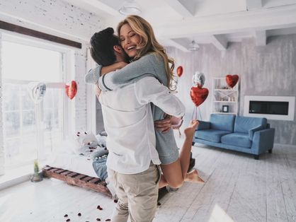 Casal se abraça em quarto decorado com balões vermelhos em formato de coração