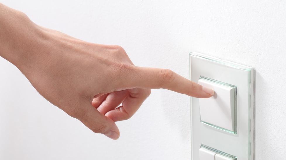 Mão de uma mulher branca com o dedo indicador apontado para um interruptor.