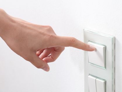 Mão de uma mulher branca com o dedo indicador apontado para um interruptor.