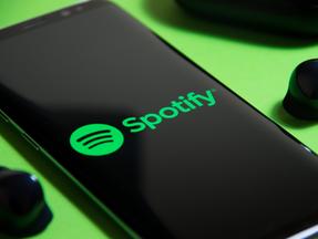 Celular ligado no aplicativo Spotify. Fundo verde e preto.