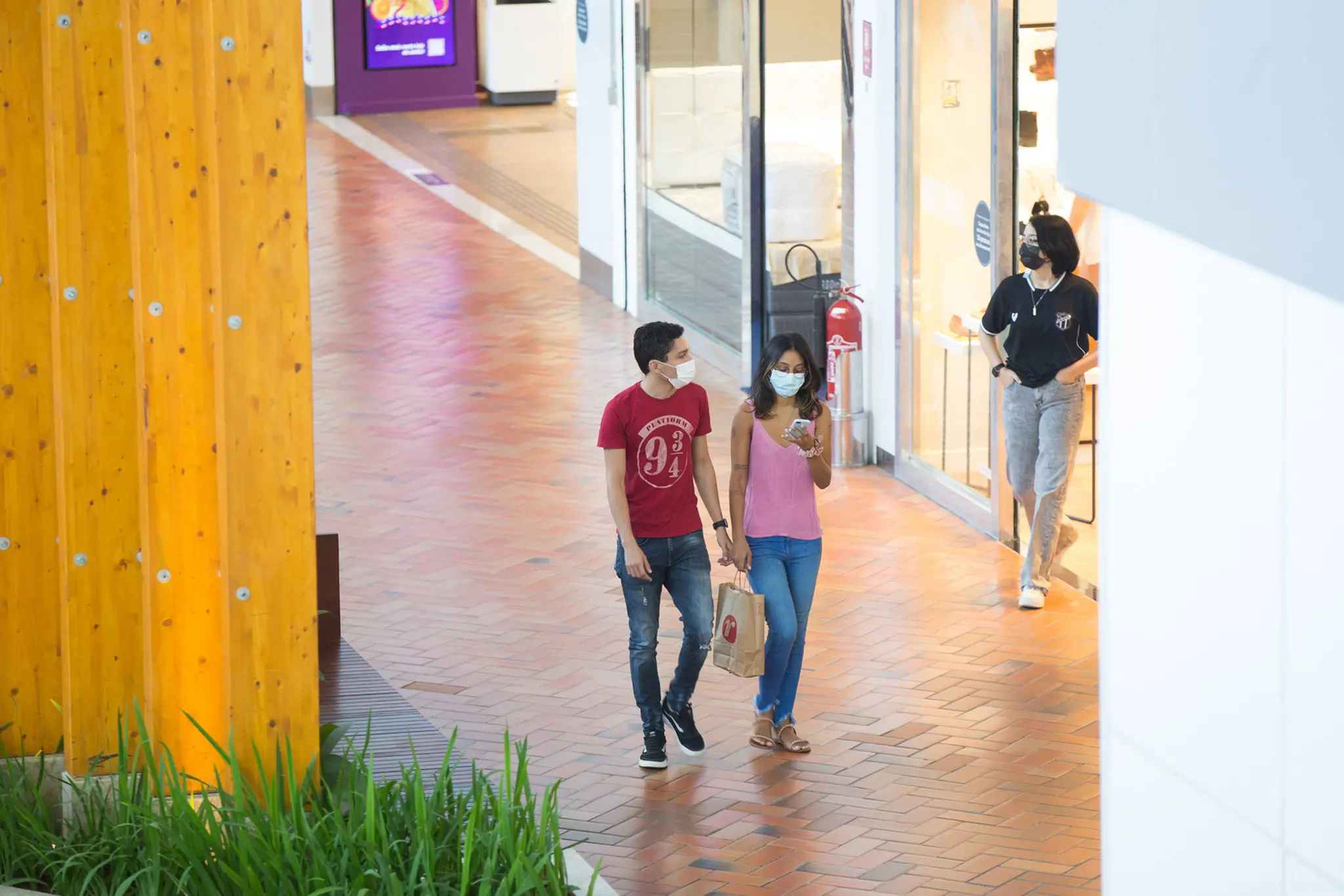 Três pessoas usam máscara contra a Covid-19 enquanto passeiam em shopping de Fortaleza