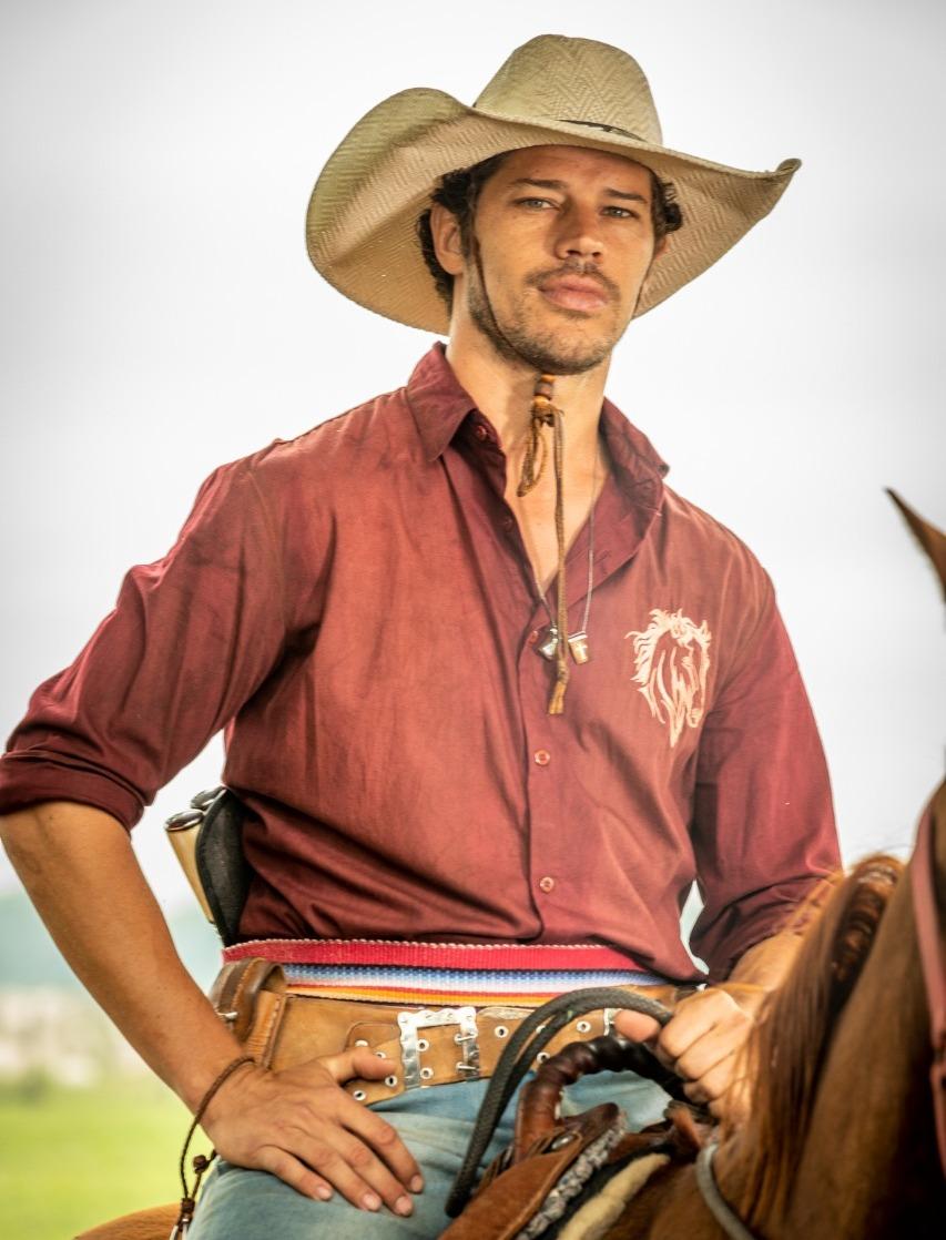 O personagem Tadeu, de Pantanal, vivido pelo ator José Loreto, está montado em um cavalo. Ele usa uma camisa vermelha e um chapéu de palha.