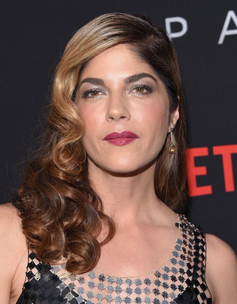 A atriz Selma Blair de frente. Ela está maquiada e usa um vestido preto em transparência e com lantejoulas.