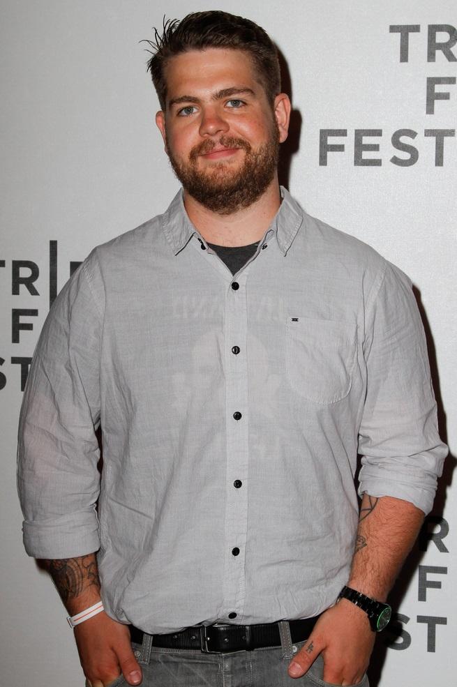 Jack Osbourne está de camisa cinza e com as mãos nos bolsos da calça. Ele é loiro e tem barba.