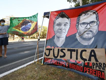 Um homem segura uma bandeira brasileira tingida de vermelho representando sangue ao lado de uma faixa exigindo justiça pela morte do jornalista britânico Dom Phillips e do indigenista brasileiro Bruno Pereira, durante um protesto em Brasília, em 19 de junho de 2022