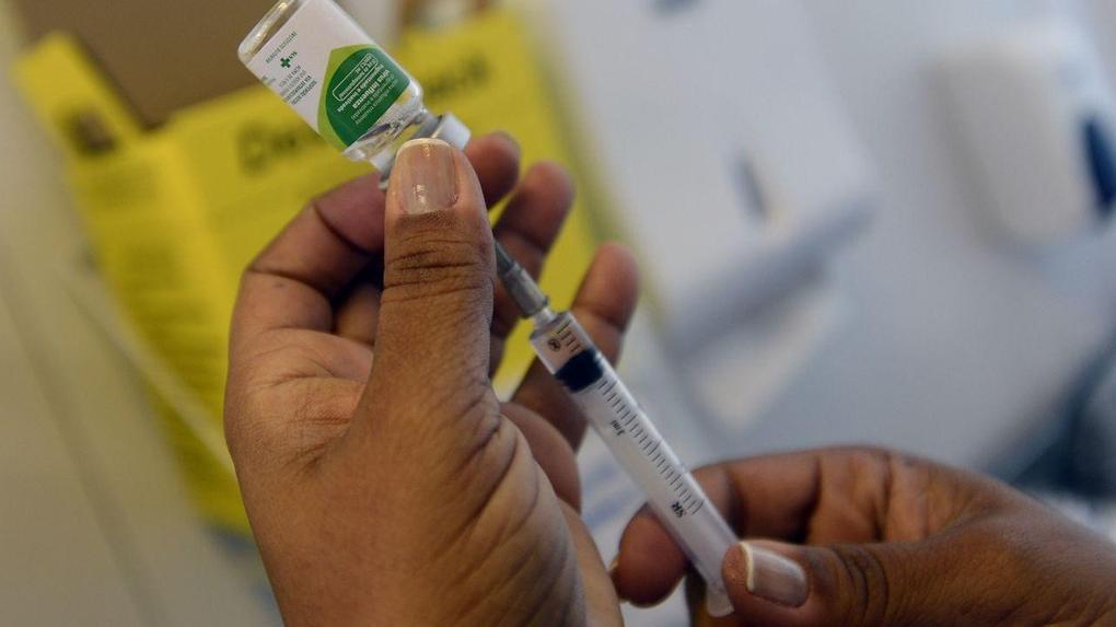 enfermeira segurando frasco de vacina contra a influenza e retirando o imunizante com uma seringa