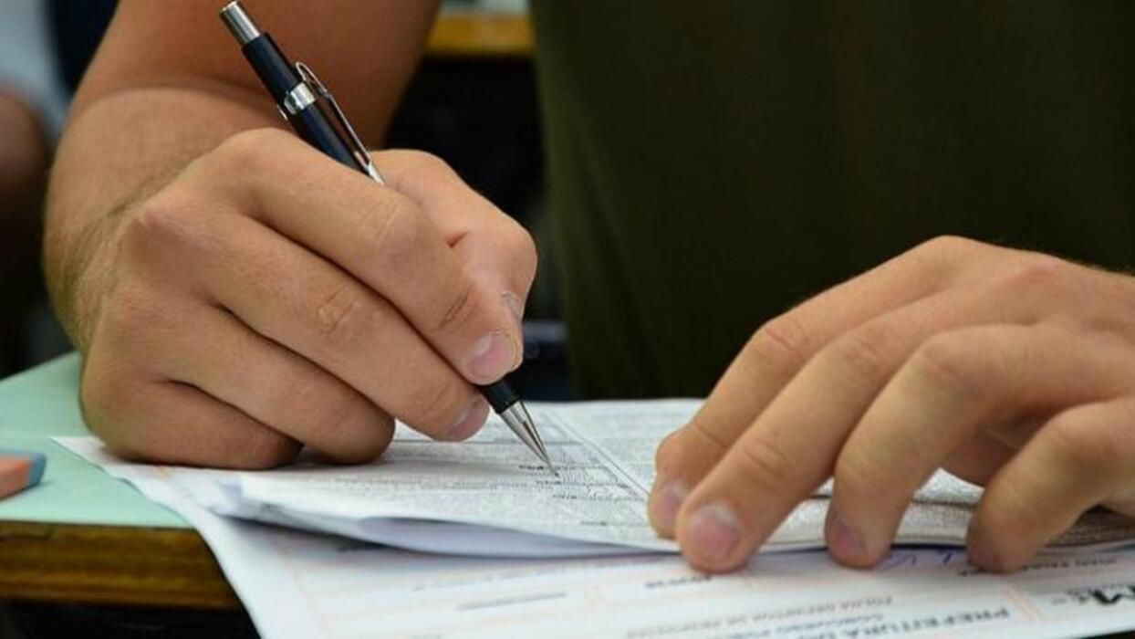Mão escreve com caneta em um pedaço de papel.
