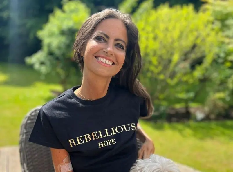 A apresentadora Deborah James de camisa preta. Ela tem cabelos pretos, olhos claros e está sorrindo para a foto.