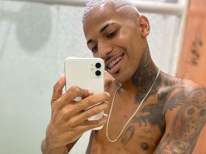 O dançario de brega-funk Jadson Neiff tira uma selfie de frente para o espelho e mostra a língua. Ele tem tatuagens e o cabelo descolorido.
