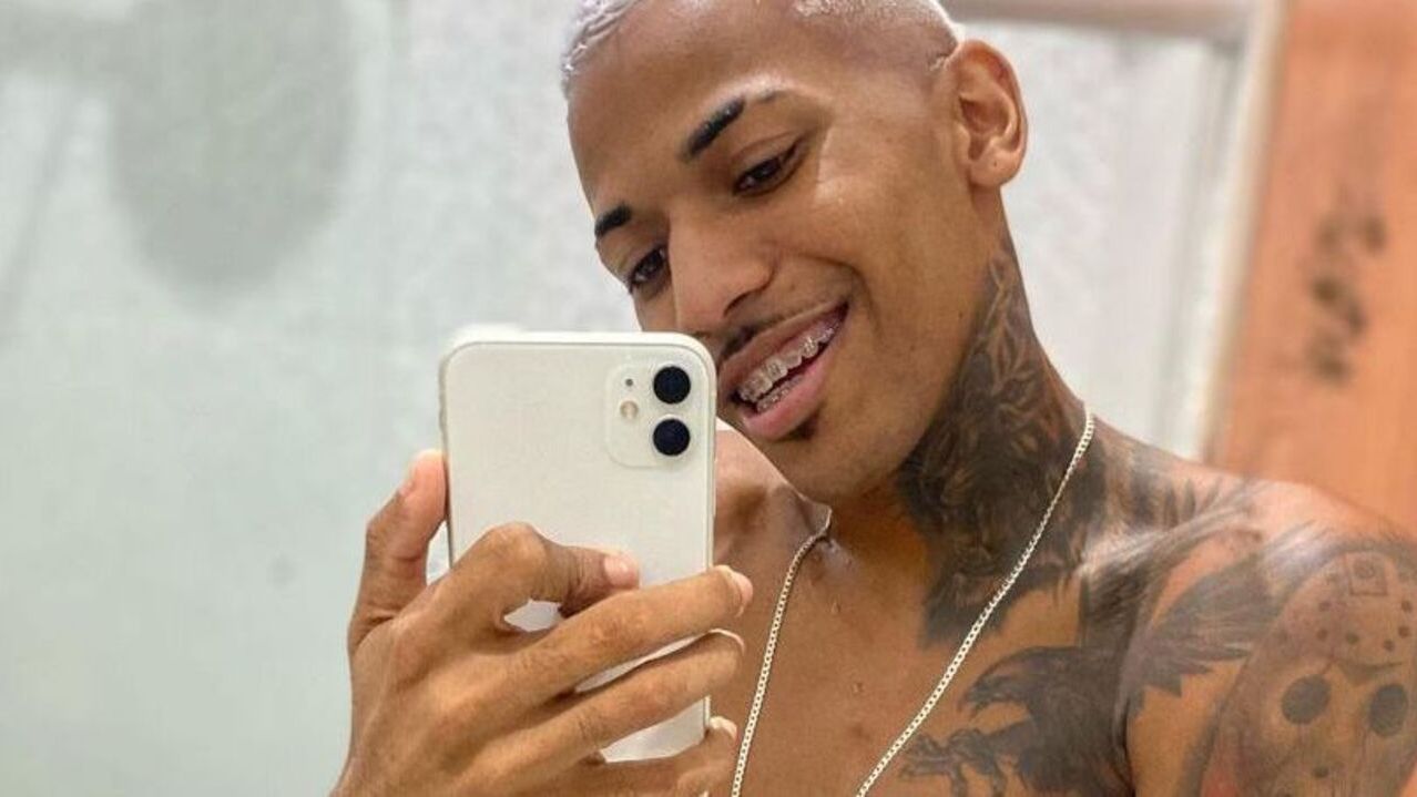 O dançarino de brega-funk Jadson Neiff tira uma selfie de frente para o espelho e mostra a língua. Ele tem tatuagens e o cabelo descolorido.