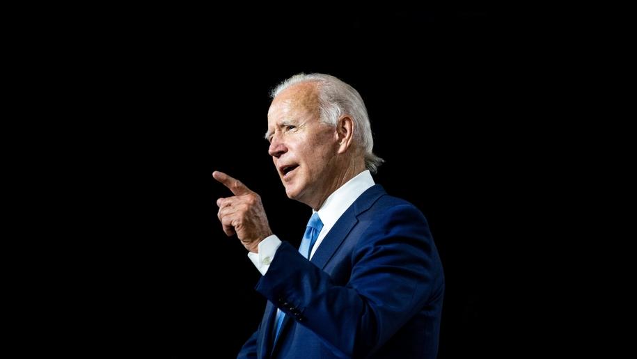 O presidente dos EUA, Joe Biden, está de terno azul e gravata azul. Ele está apontando com o dedo indicador para frente.