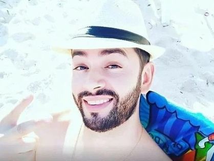 O agente penal Jorge Guaranho está em uma praia. Ele usa um chapéu branco de palha.
