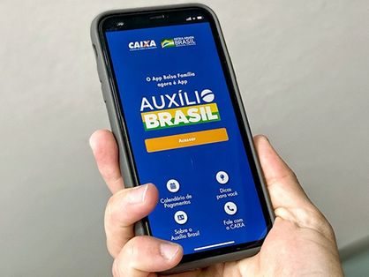 Close em uma mão masculina que segura smartphone com o aplicativo do Auxílio Brasil aberto