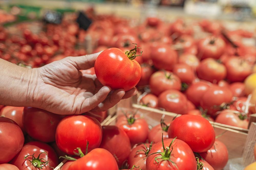 Mão segura um tomate em uma seção no supermercado.
