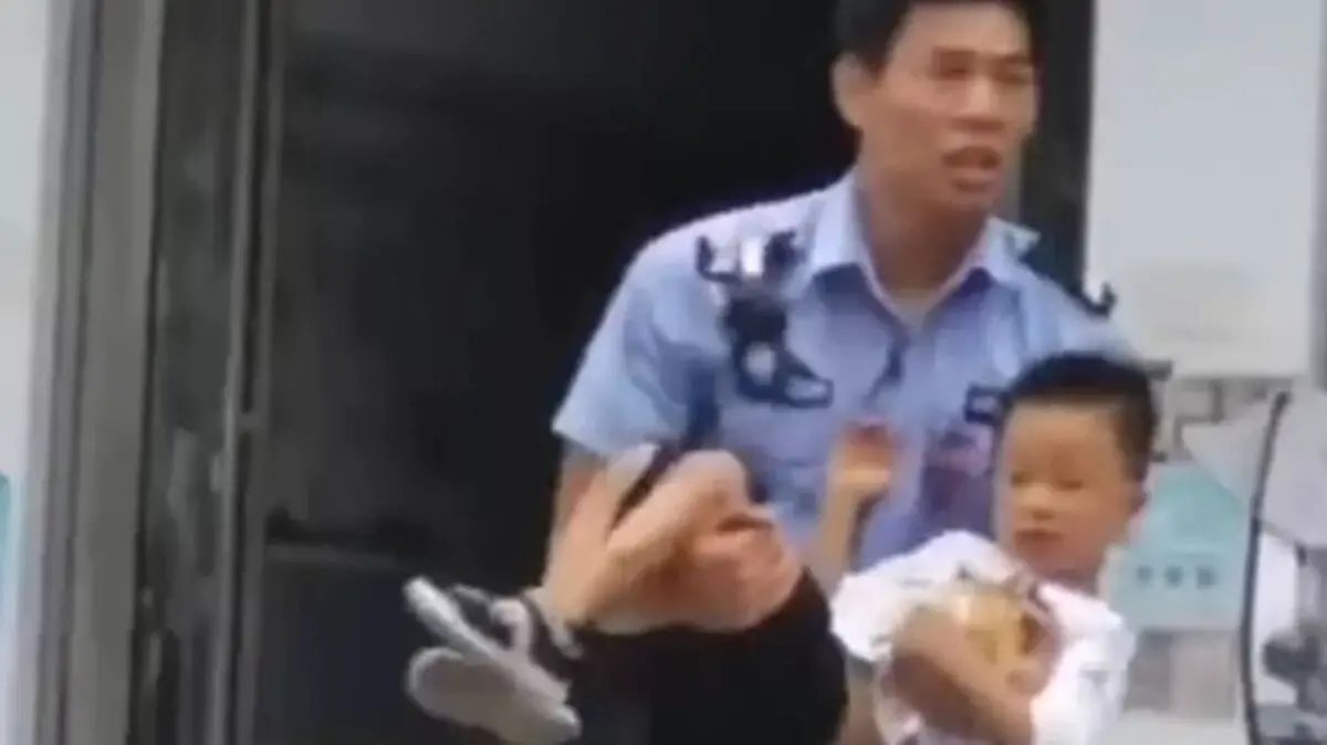Policial chinês segura criança no colo. Eles estão saindo da creche onde um homem entrou e esfaqueou pessoas.