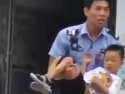 Policial chinês segura criança no colo. Eles estão saindo da creche onde um homem entrou e esfaqueou pessoas.