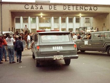 Fachada da Casa de Detenção Carandiru, em São Paulo. Carros e profissionais da imprensa aparecem na imagem.