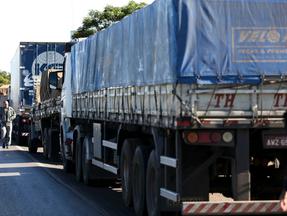Caminhoneiros transitam ao lado de fileira de caminhões parados no acostamento de uma rodovia