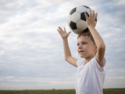 Criança segura bola em campo
