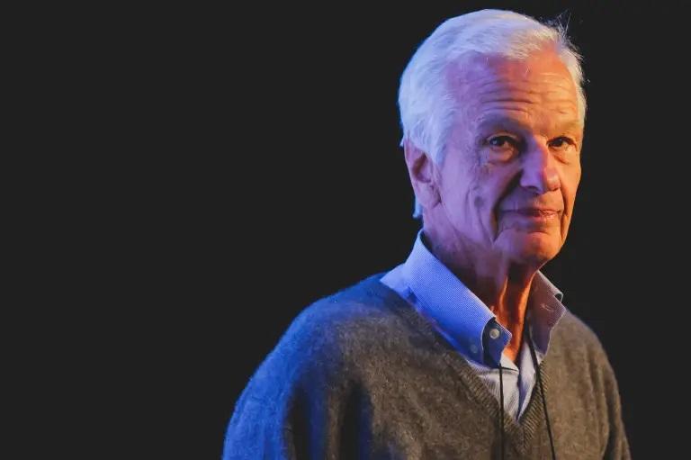 Jorge Paulo Lemann é um homem idoso, branco, de cabelos grisalhos. Ele está olhando sereno. Veste uma camisa de botão por baixo de um pulôver.