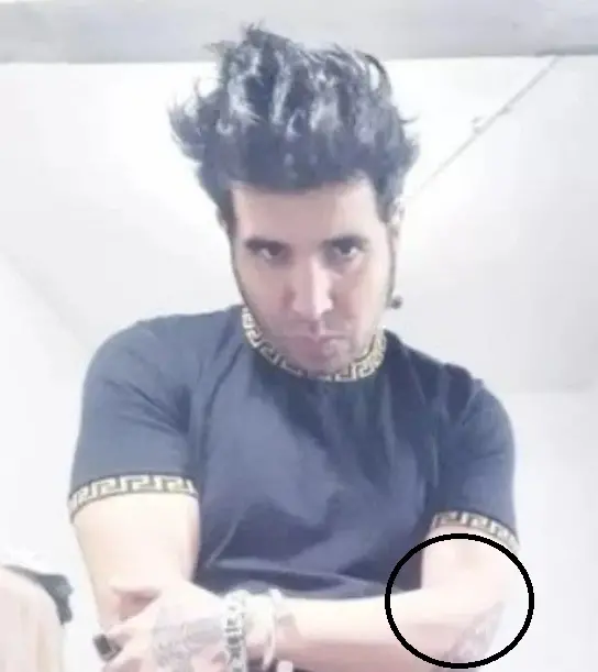 Fernando Andrés é um homem branco, de cabelos pretos espetados. Ele está usando uma camisa preta. Há um círculo marcado sobre o símbolo 