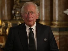 O rei Charles III é um homem branco e de cabelos brancos. Ele usa um terno preto e uma gravata da mesma cor.