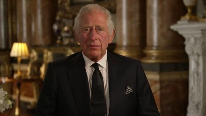 O rei Charles III é um homem branco e de cabelos brancos. Ele usa um terno preto e uma gravata da mesma cor.