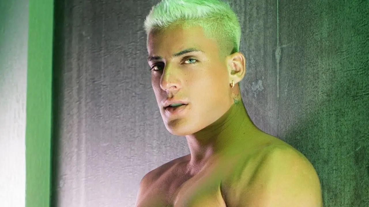 Tiago Ramos é um homem branco e está usando o cabelo platinado. Ele está sem camisa e olhando para a câmera.