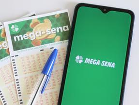 Papel de loteria e celular aberto no aplicativo da Mega-Sena.