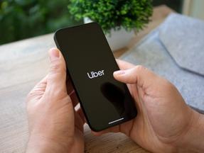 Mão de homem segurando o iPhone 13 Pro Graphite com aplicativo Uber na tela.