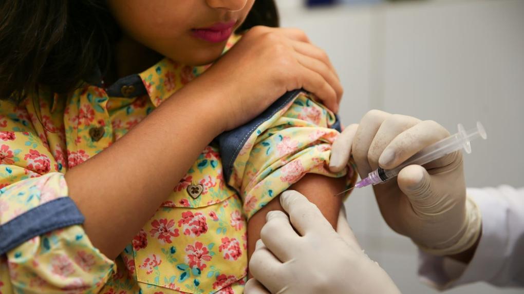 vacina sendo aplicada em braço de menina com roupa amarela estampada