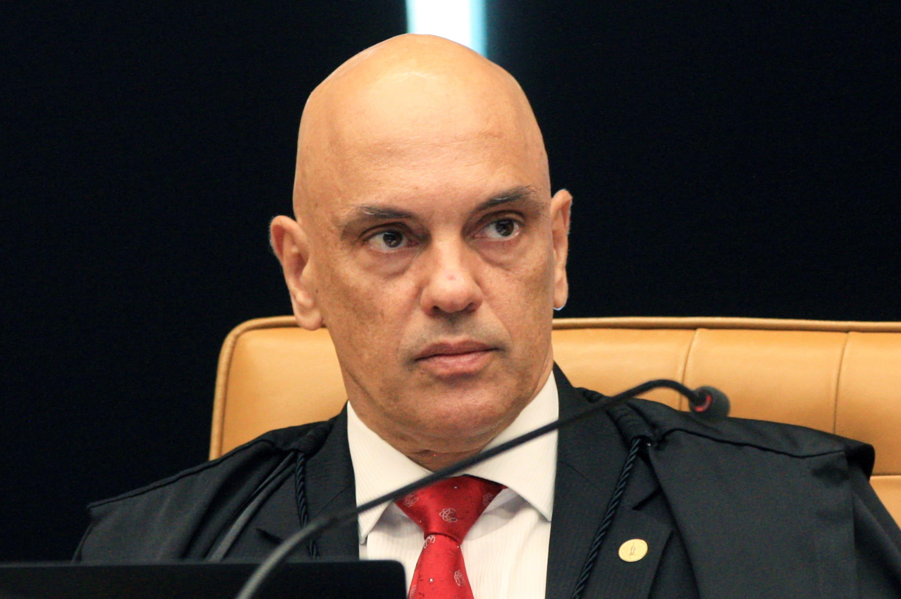 O ministro Alexandre de Moraes é um homem branco e careca. Ele veste terno preto e gravata vermelha. Sua expressão é séria.