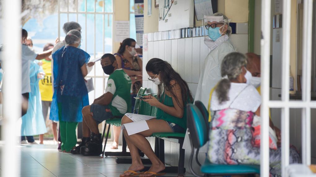 Imagem mostra recepção de posto de saúde com pacientes e profissionais da saúde em Fortaleza