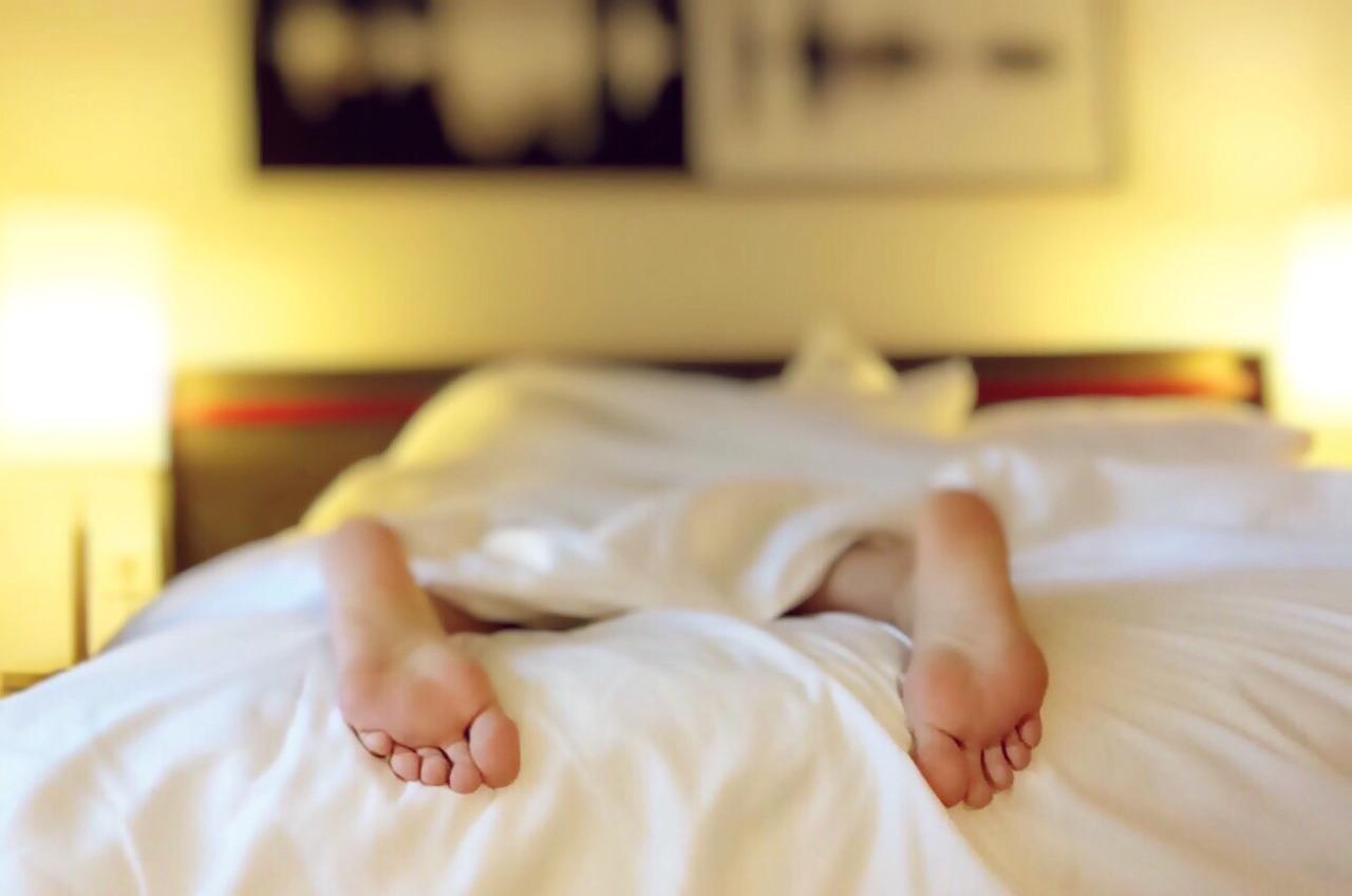 Pessoa dorme de barriga para baixo em uma cama. Em destaque, estão seus pés virados para baixo