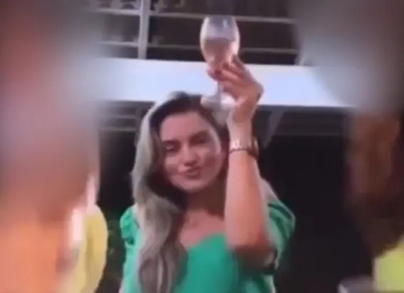Advogada veste verde e segura taça com vinho rosé. Ela é branca e loira