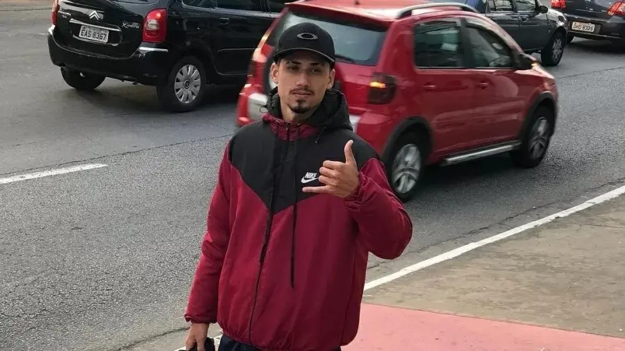 Briner é um homem negro, de barba desenhada. Na foto, ele está com um casaco vermelho, um boné preto e fazendo sinal de hang loose com a mão