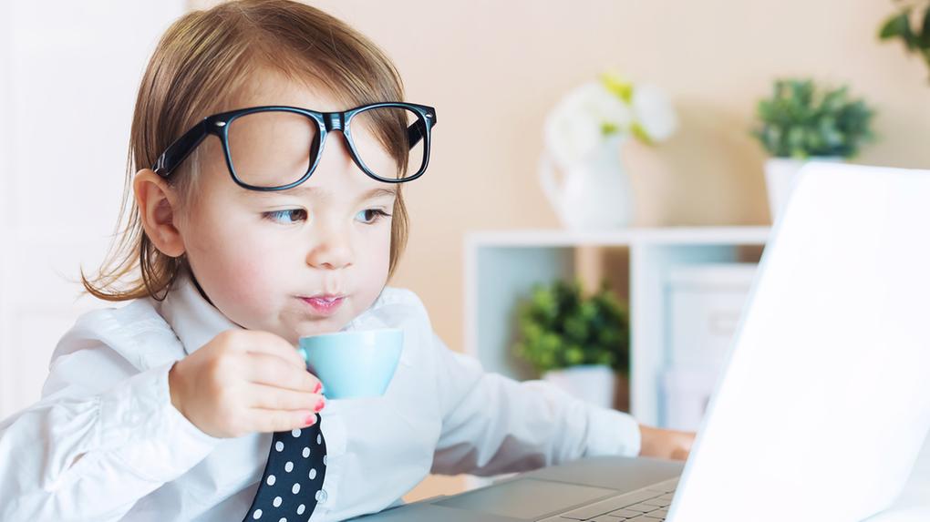 criança em frente ao computador com uma pequena xícara de café e óculos na testa
