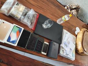 Objetos dispostos sobre uma mesa. Há celulares, dinheiro em espécie, uma garrafa d'água e documentos.