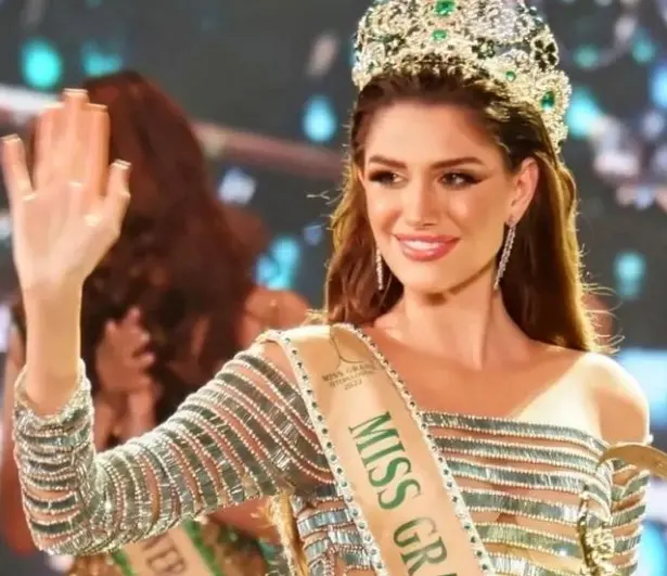 Isabella Menin com uma coroa e uma faixa de vencedora do concurso de beleza. Ela é uma mulher branca, magra e tem os cabelos longos e castanhos escuros.