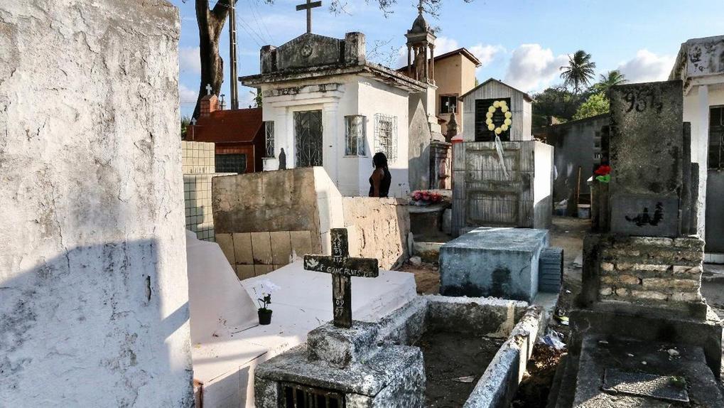 Mulher caminha solitária por entre lápides de cemitério em Fortaleza.