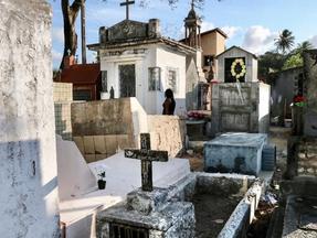 Mulher caminha solitária por entre lápides de cemitério em Fortaleza.