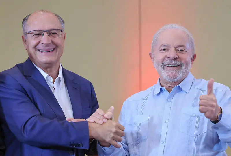 Geraldo Alckmin e Lula. Os dois estão sorrindo e de mãos dadas.