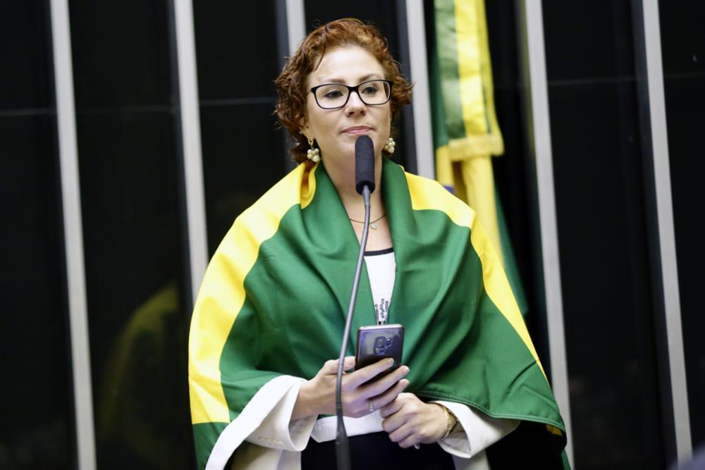 A deputada Carla Zambelli está com uma bandeira do Brasil sobre os ombros.
