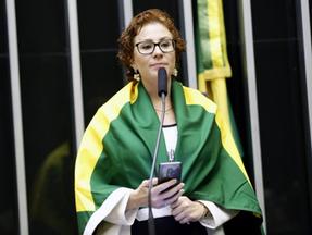A deputada Carla Zambelli está com uma bandeira do Brasil sobre os ombros.