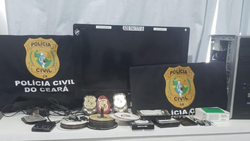 Material apreendido pela Polícia Civil. Sobre a mesa, há CDs, pendrives, celulares e computadores