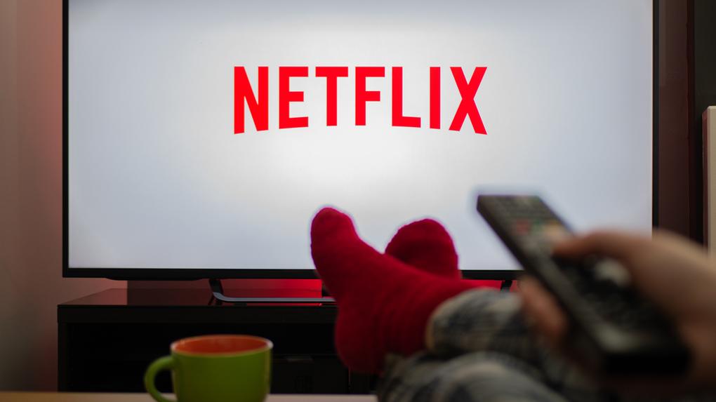 Televisão com logotipo da Netflix e pessoa assistindo com os pés para cima em uma confortável casa