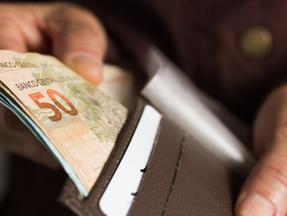 Mão masculina guarda cédulas de 100 e 50 reais em uma carteira marrom