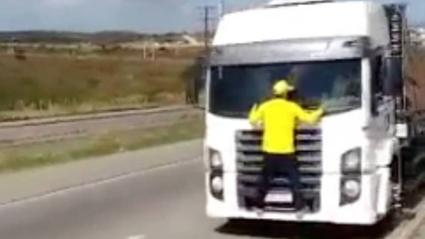 Bolsonarista de camisa amarela e boné da mesma cor pendurado na frente de caminhão em movimento