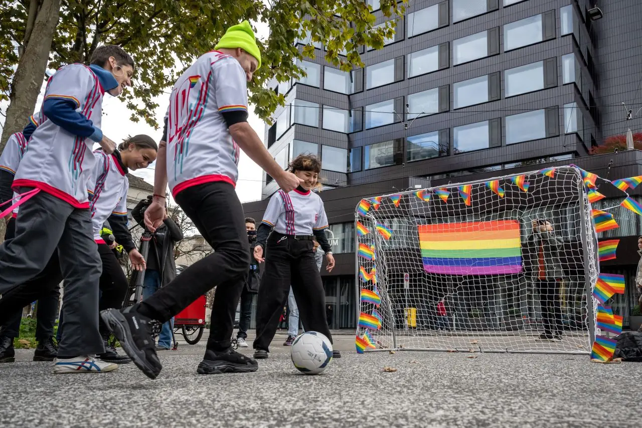 pessoas jogam futebol com bandeira lgbt pendurada em trave de gol